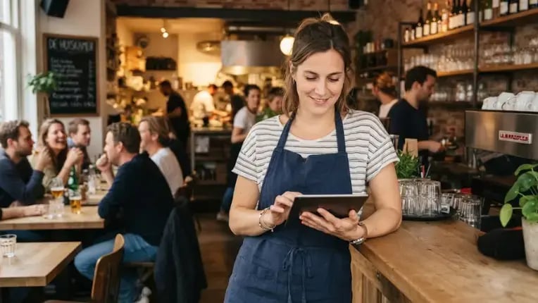 Horecaondernemer regelt ontspannen haar personeelszaken op een tablet achter de bar van haar café.