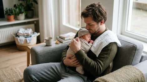 Vader houdt zijn pasgeboren baby in zijn armen tijdens het geboorteverlof thuis op de bank
