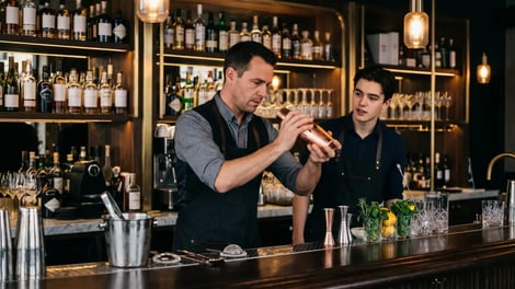 Ervaren bartender leert een jongere collega cocktails maken achter een sjieke bar