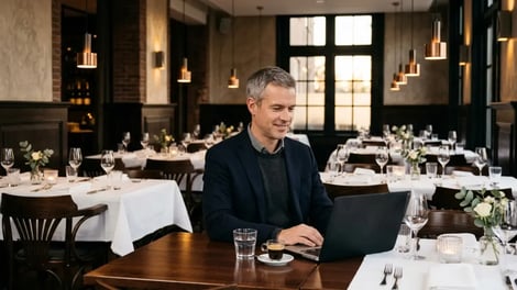 Restauranteigenaar werkt op zijn laptop tussen gedekte tafels in zijn restaurant